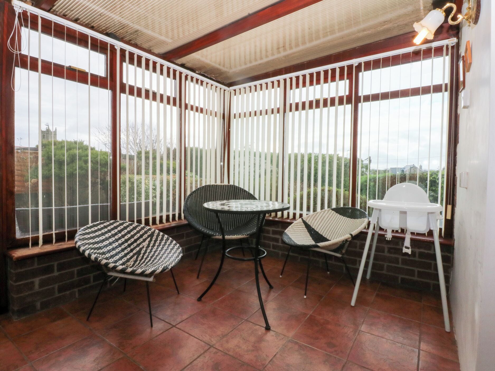 Un patio en esquina con pared de ladrillo, una mesa redonda, dos sillas y una trona blanca para bebé.