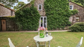Un pequeño espacio exterior con una mesa redonda y dos sillas, un florero con flores y una botella de champán.