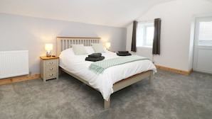 Quarto com cama, mesas de cabeceira, radiador, janela com cortinas e luminária pendente.