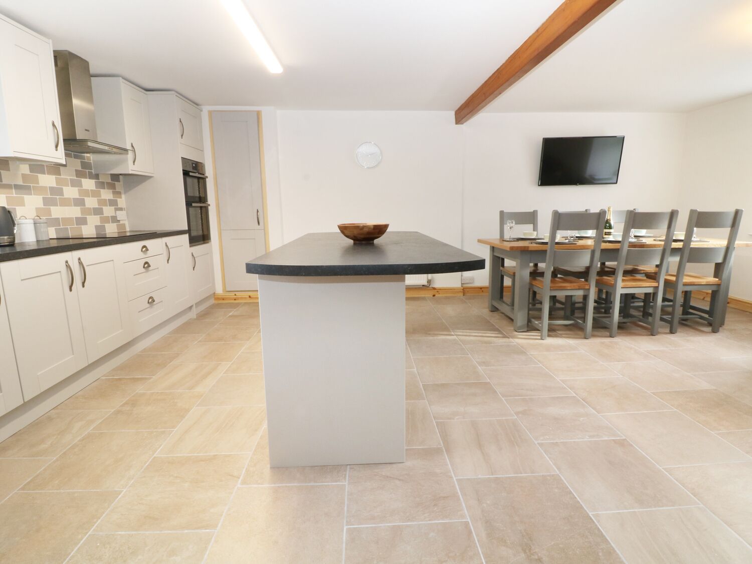 A modern kitchen with white cabinets, a central island, and a dining area with a wooden table and chairs.