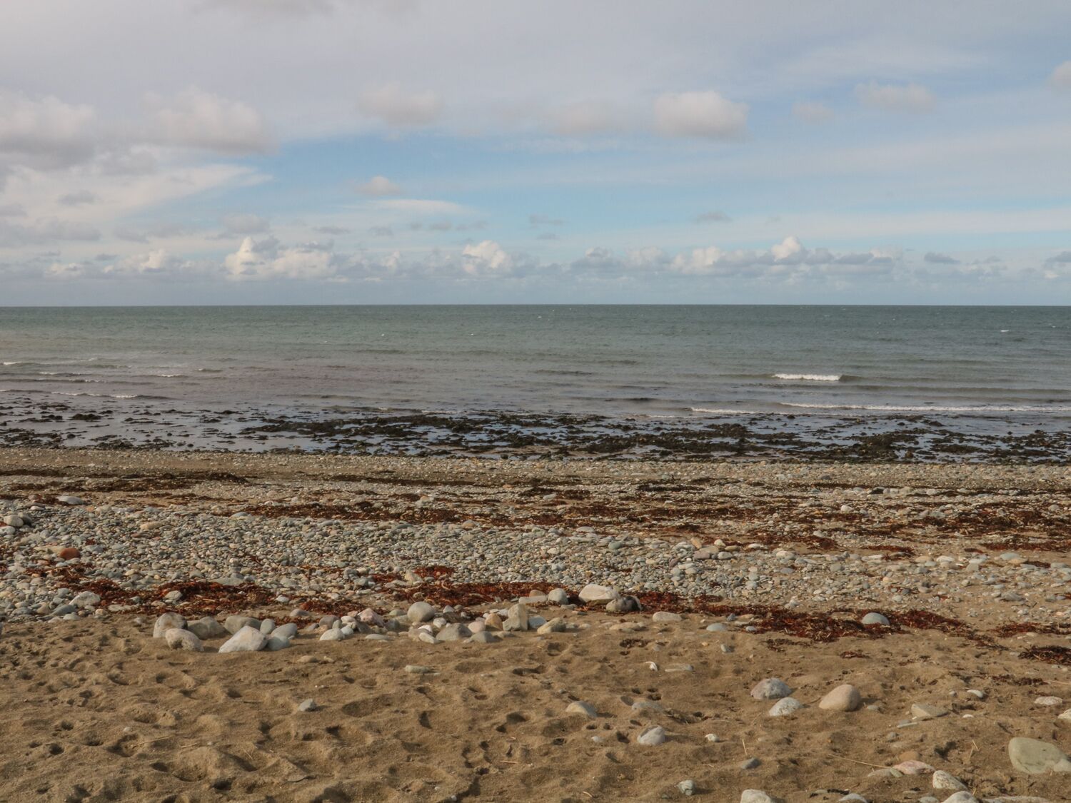 A beach with pebbles and seaweed, leading to the ocean.