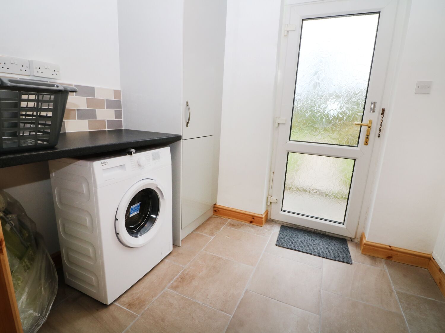 Une buanderie équipée d’un lave-linge à chargement frontal, d’une petite poubelle et d’une porte dont les panneaux sont en verre dépoli.