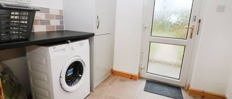 Une buanderie équipée d’un lave-linge à chargement frontal, d’une petite poubelle et d’une porte dont les panneaux sont en verre dépoli.