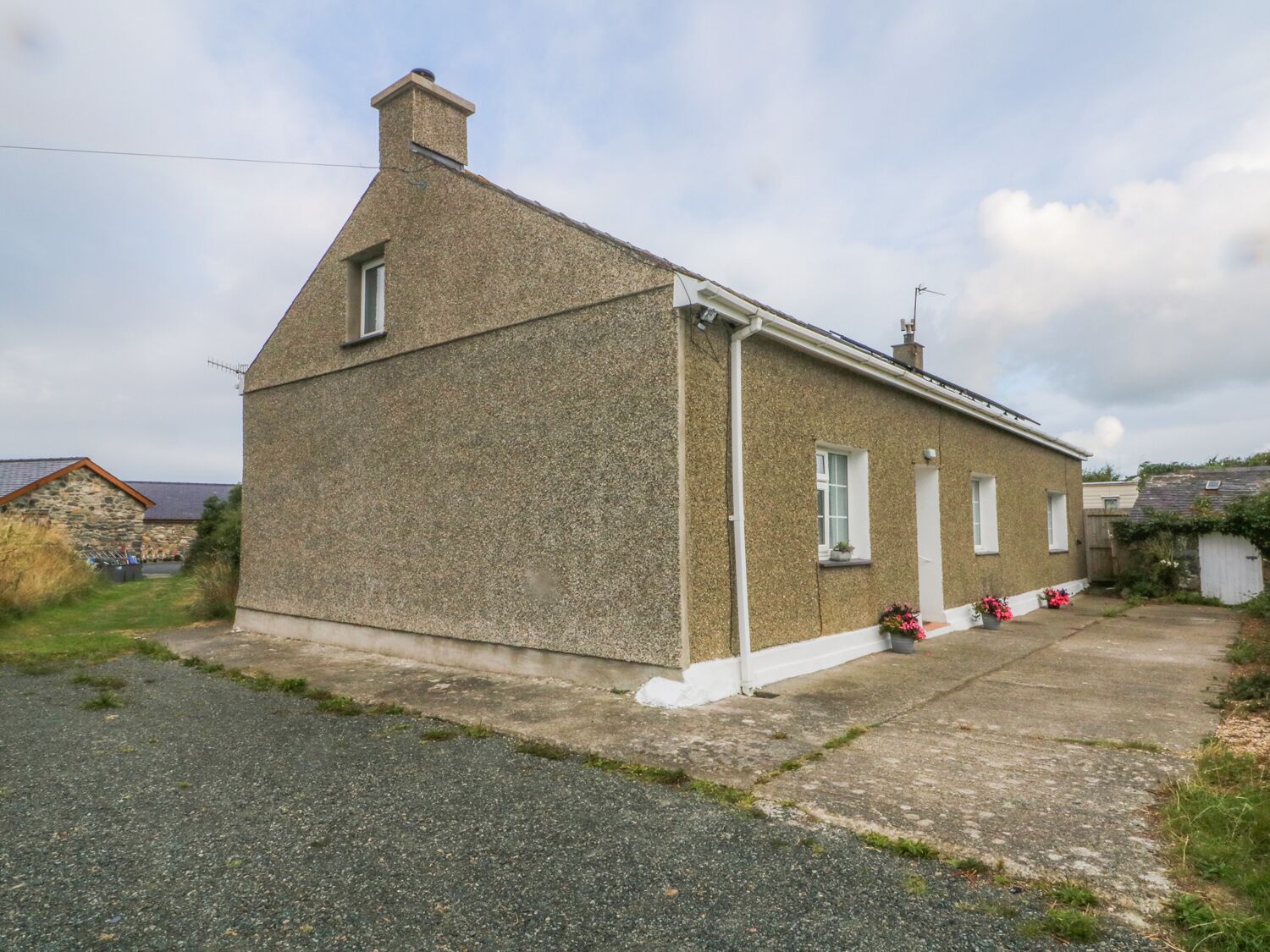 A single-story house with a sloped roof, a chimney, and a small porch with potted plants.