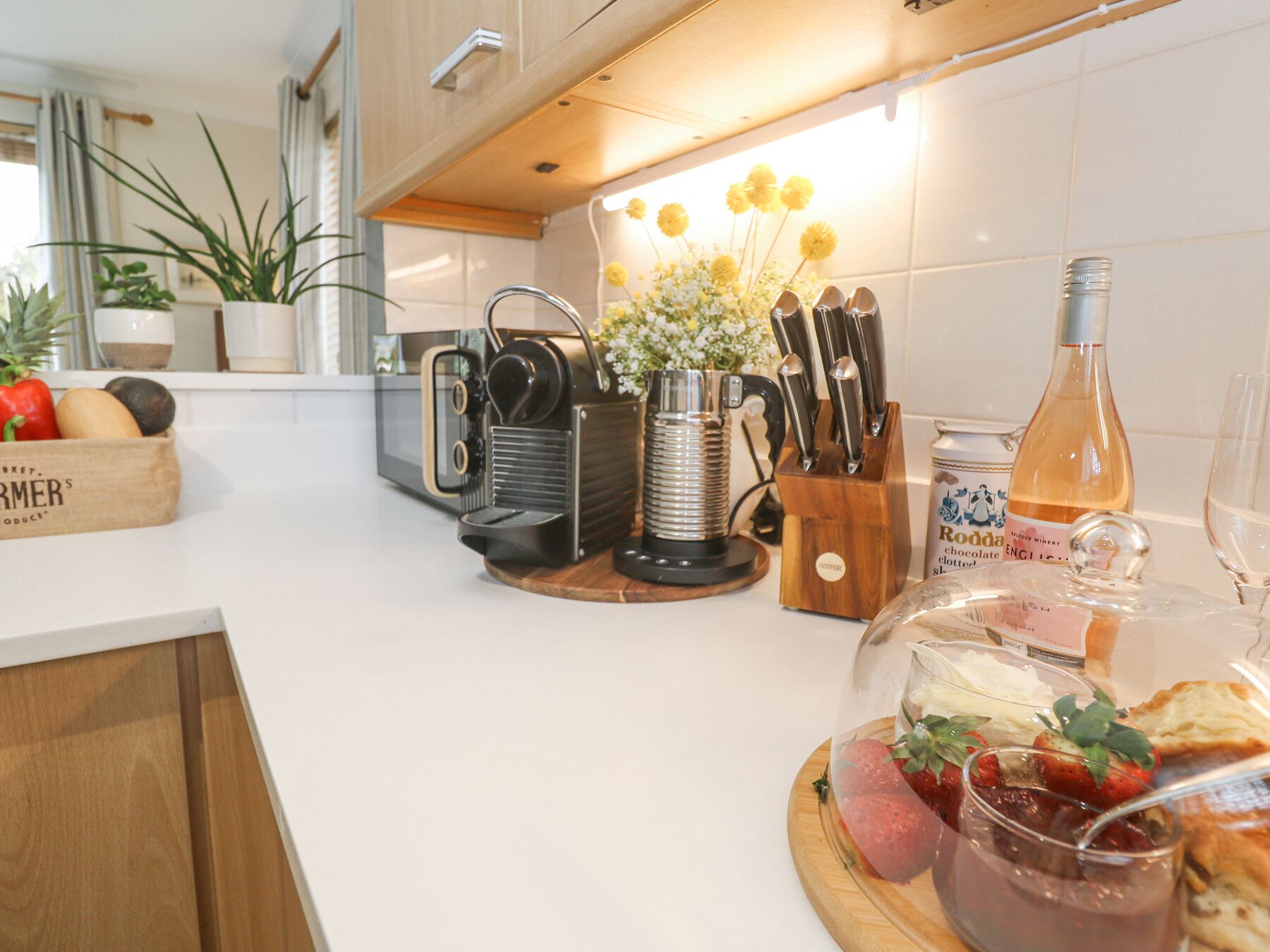A modern kitchen with a coffee machine, a knife block, a bottle of wine, and a fruit platter.