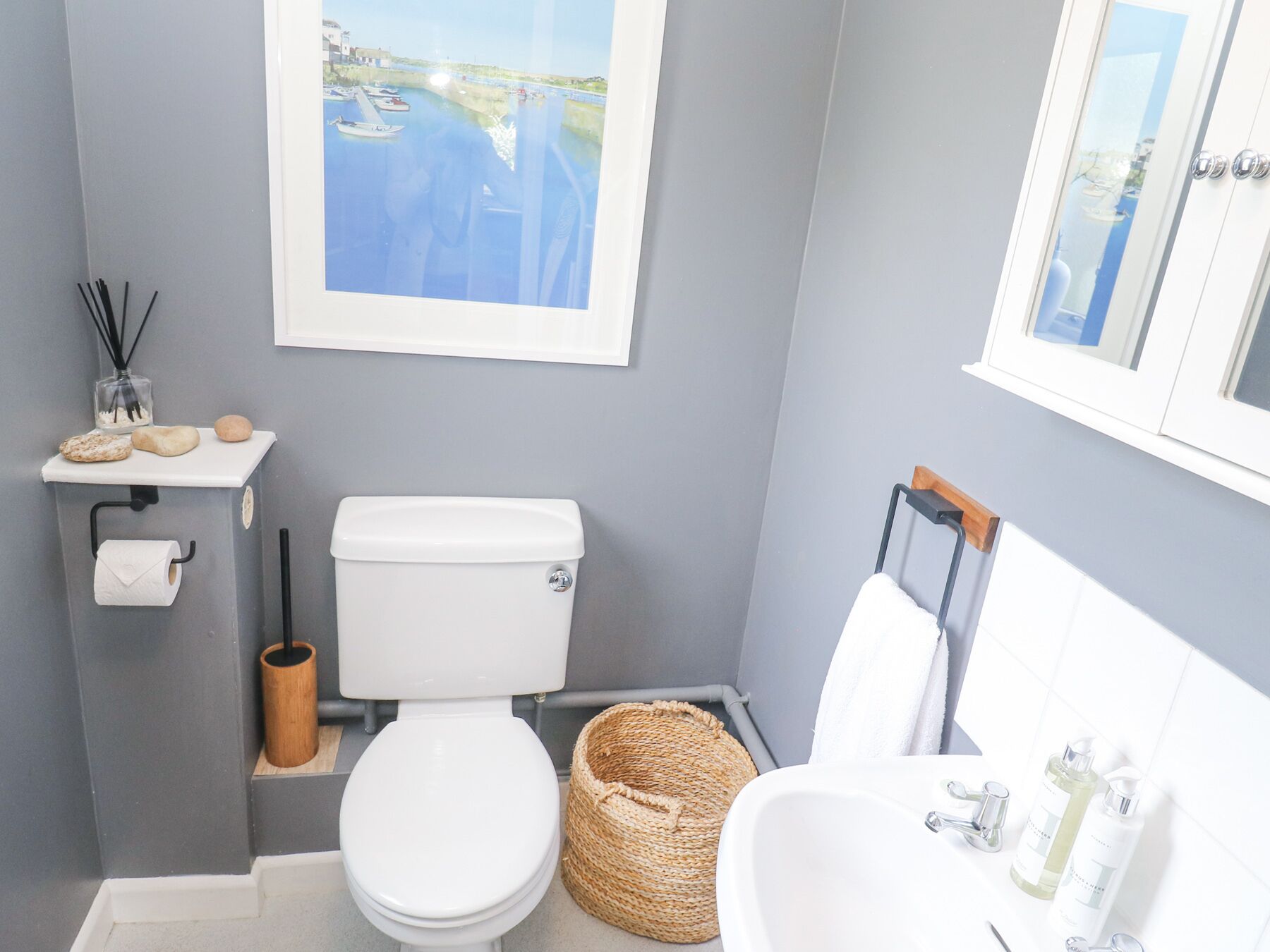 A bathroom with a toilet, sink, and a framed picture of a water body.