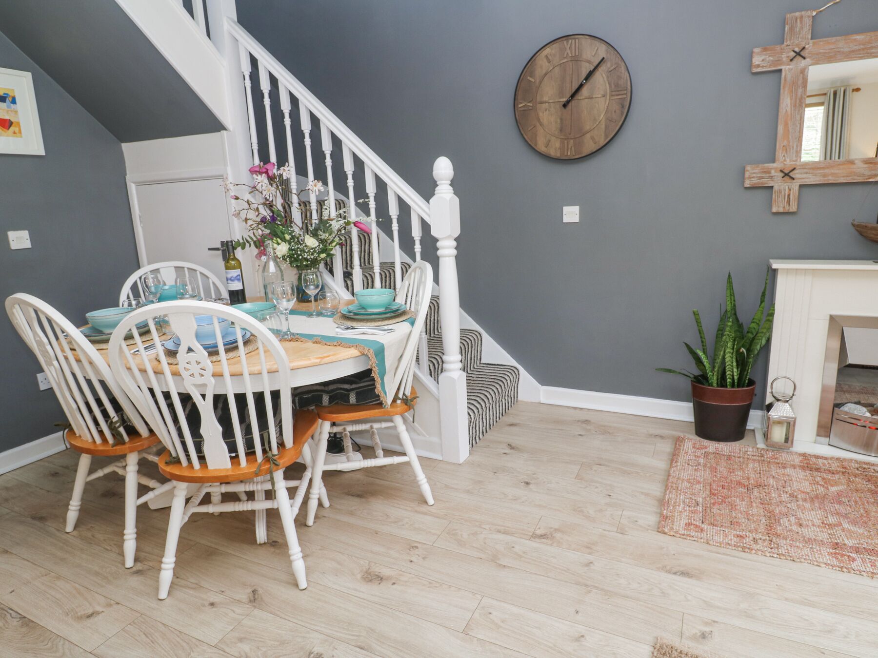 A dining area with a wooden table, white chairs, and a grey wall with a wooden clock.