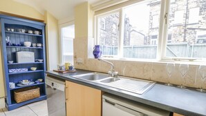 A kitchen with a built-in dishwasher, a double sink, and a window overlooking a brick building. - The Garden Flat (Harrogate)