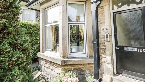 A corner building with a stone facade, a black door labeled "Edina Ville," and a window with a white frame. - The Garden Flat (Harrogate)