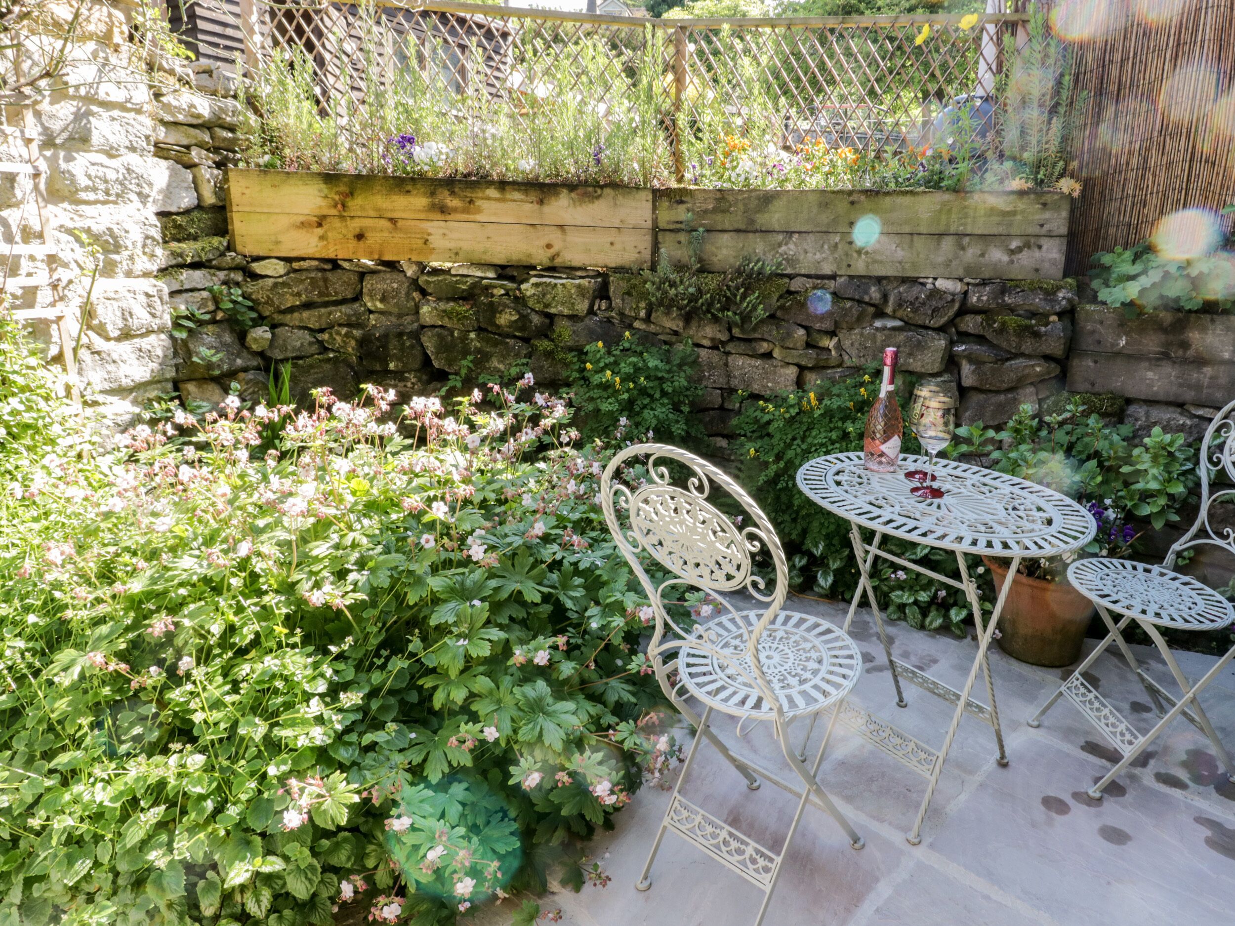 A stone wall with a wooden planter box, surrounded by lush greenery and pink flowers.