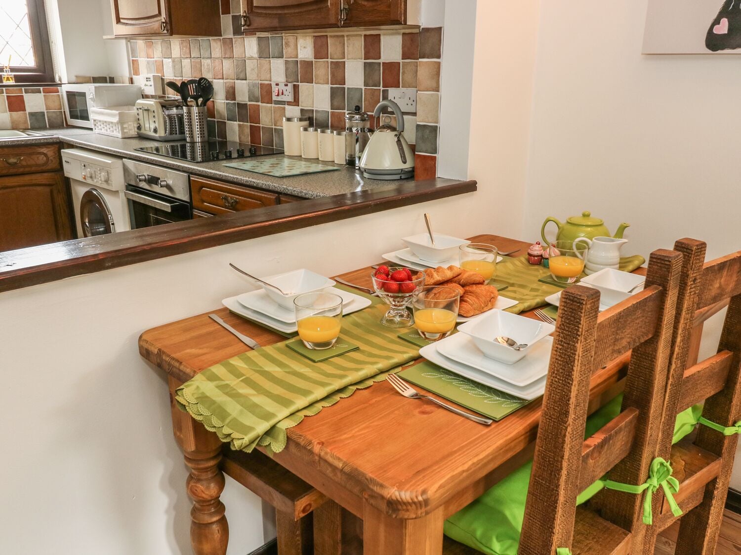 Un desayuno preparado con una mesa para dos personas, incluyendo platos, vasos y un bol de fresas.