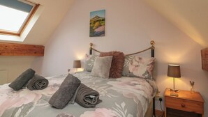 A bedroom with a sloped ceiling, a bed with floral bedding, two bedside lamps, and a painting on the wall.