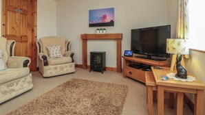 A living room with a sofa, armchair, TV, fireplace, and a painting on the wall.