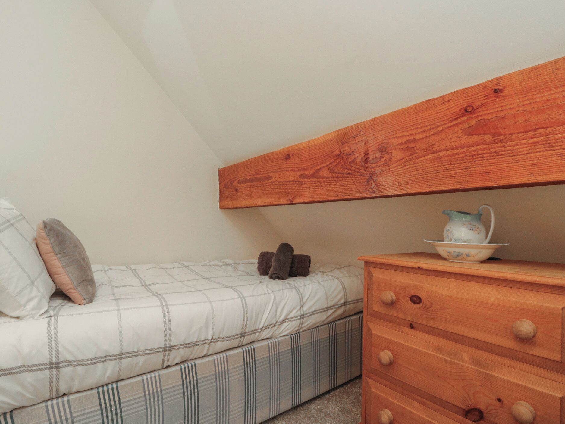 A bedroom with a bed, a wooden dresser, and a small table with a pitcher.