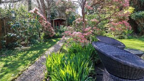 Un jardin avec un sentier, une petite construction et des meubles en osier.