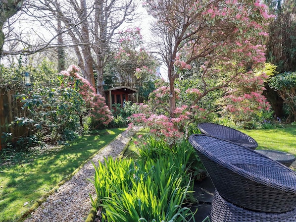 Un jardin avec un sentier, une petite construction et des meubles en osier.