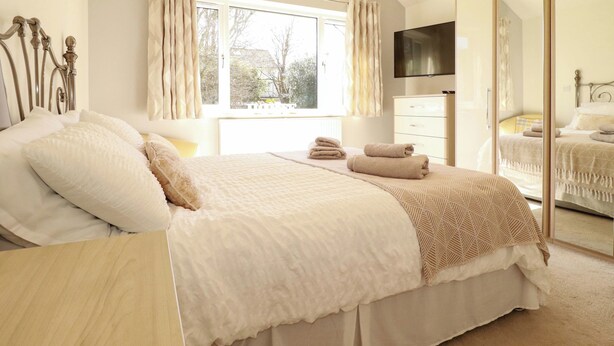 Une chambre à coucher avec un lit, une commode, un miroir et une fenêtre avec des rideaux.