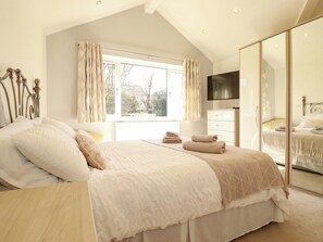 Une chambre à coucher avec un lit, une commode, un miroir et une fenêtre avec des rideaux.