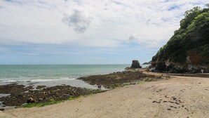 Une plage aux rivages rocheux, un ciel dégagé et une formation rocheuse visible au loin.