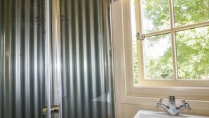 A bathroom with a white sink, a window with a view of trees, and a shower with a metal door. - Orchard (Wadebridge)