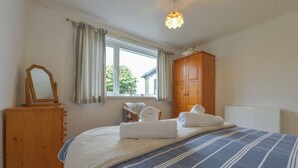 Une chambre à coucher avec un grand lit, une commode en bois, une chaise et une fenêtre avec des rideaux.