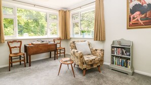 A cozy room with a wooden table, two chairs, a patterned armchair, a bookshelf, and a painting of ostriches. - Little Yaffle (Dover)