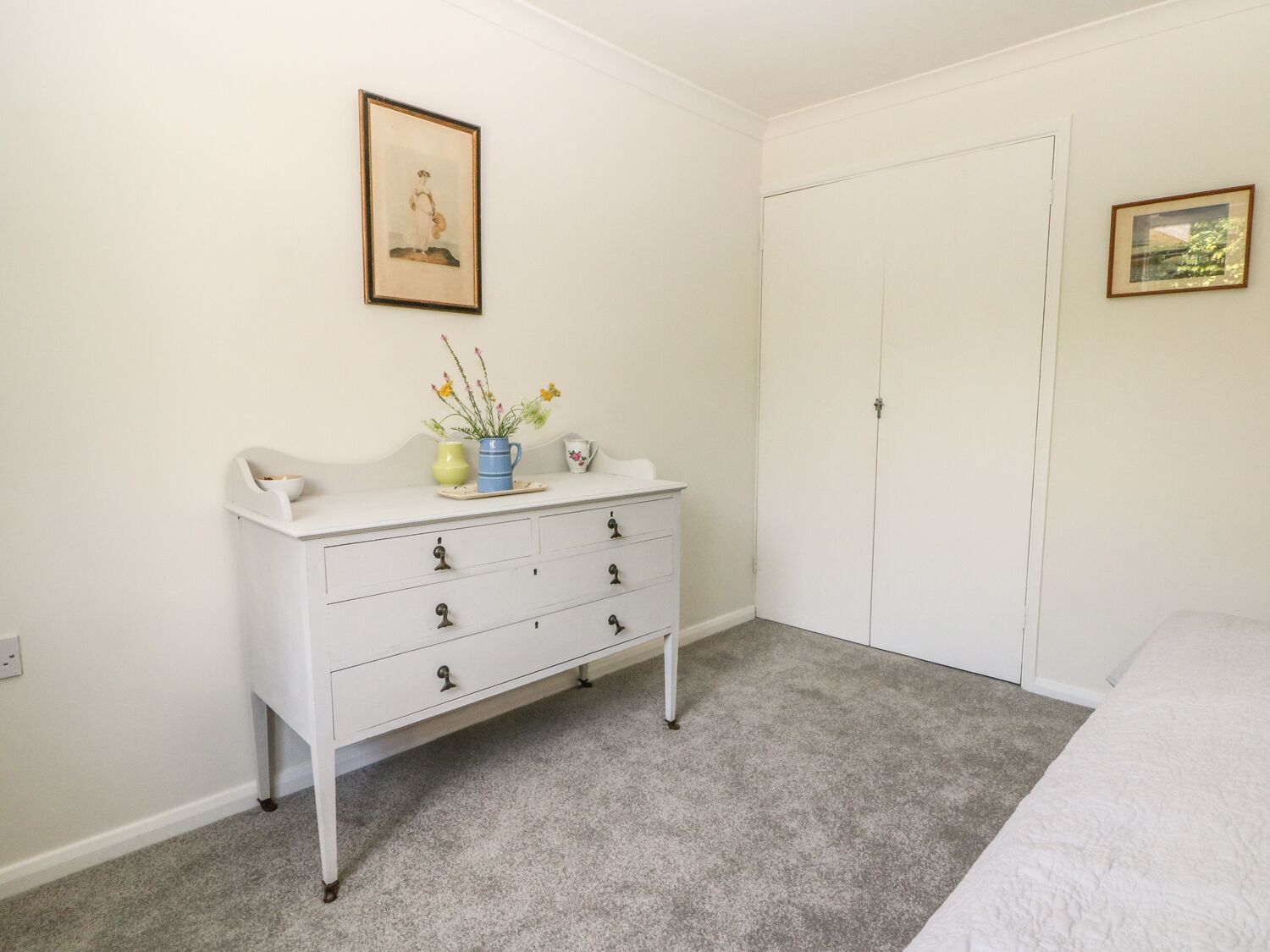 A bedroom with a white dresser, a bed, a door, and a framed picture on the wall.