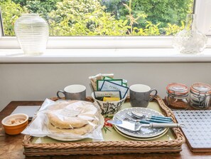 A breakfast tray with pastries, coffee, tea bags, and utensils on a table by a window with a view of greenery. - Little Yaffle (Dover)