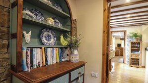 A room with a wooden bookshelf filled with books and decorative plates, a vase with flowers, and a stone wall. - The Croft (Holsworthy)