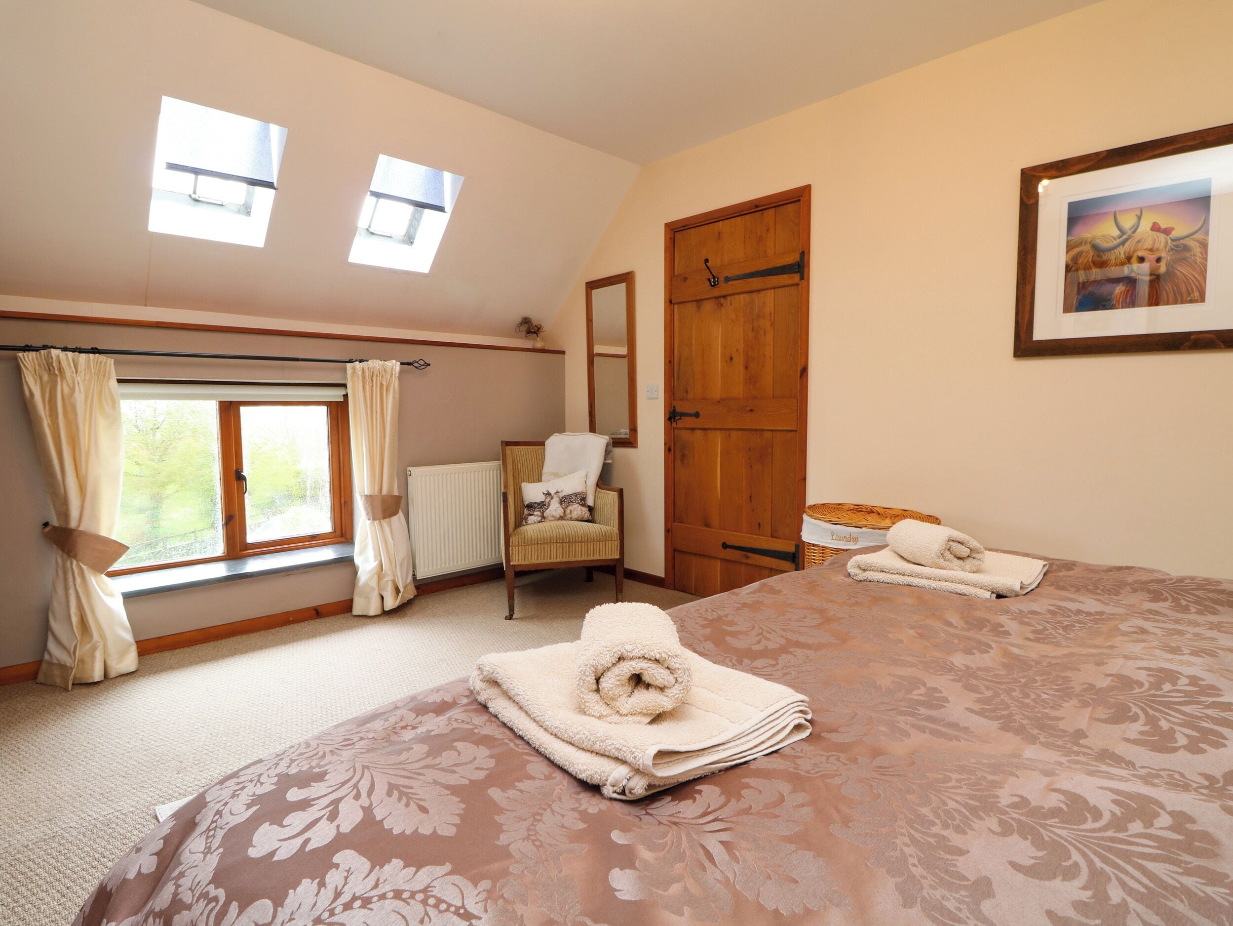 A bedroom with a large bed, two windows, a chair, a wooden door, and a framed picture on the wall.
