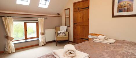A bedroom with a large bed, two windows, a chair, a wooden door, and a framed picture on the wall.