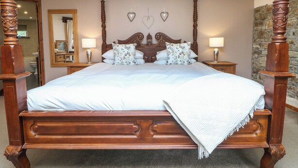 A four-poster bed with a wooden headboard, two bedside tables with lamps, and a mirror on the wall. - The Croft (Holsworthy)