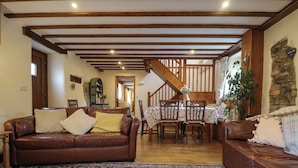 A cozy living room with a brown leather sofa, a patterned rug, and wooden beams on the ceiling. - The Croft (Holsworthy)