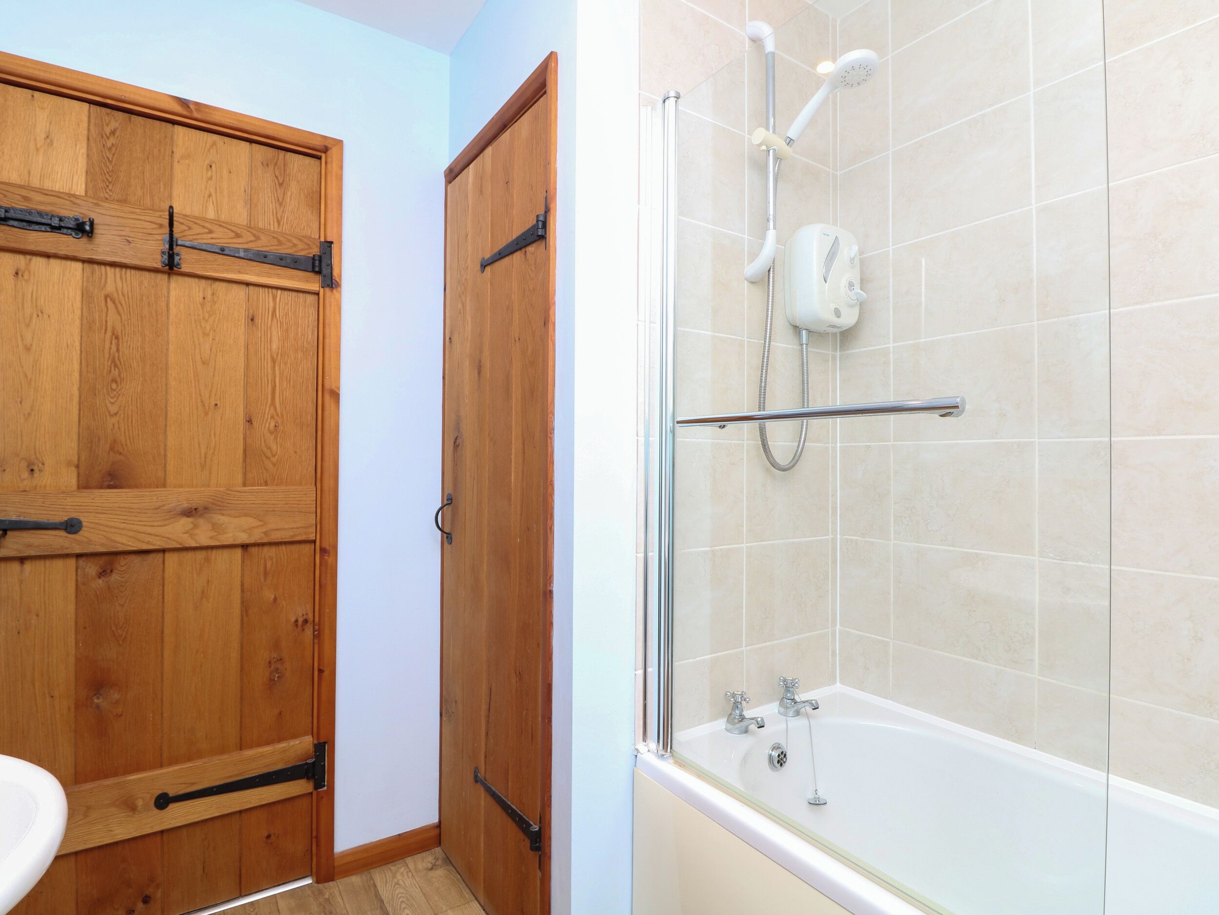 Une salle de bain avec une porte en bois, une douche dotée d’une paroi en verre et une baignoire.
