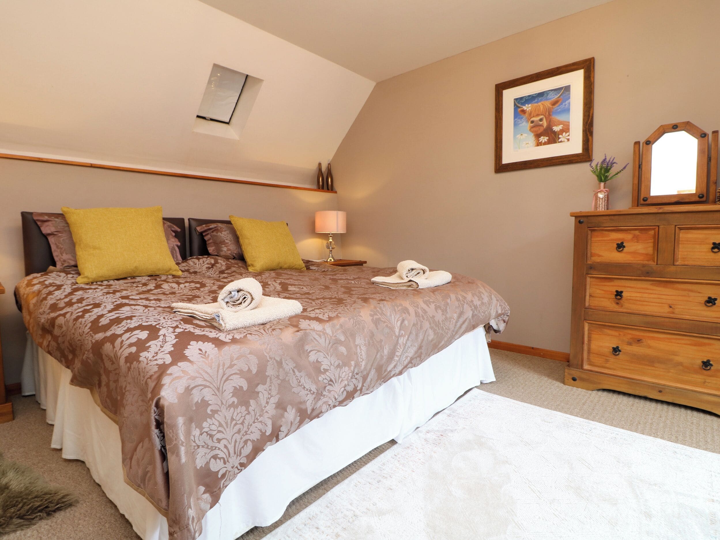 A bedroom with a large bed, a wooden dresser, a framed picture on the wall, and a small skylight.