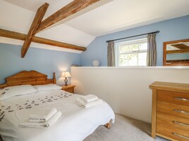 Un dormitorio con cama de madera, una mesita de noche con lámpara, un aparador y una ventana con cortinas.