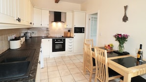 A kitchen with white cabinets, a black oven, and a dining area with a table and chairs. - Street House Farm Cottage (Saltburn-by-the-Sea)