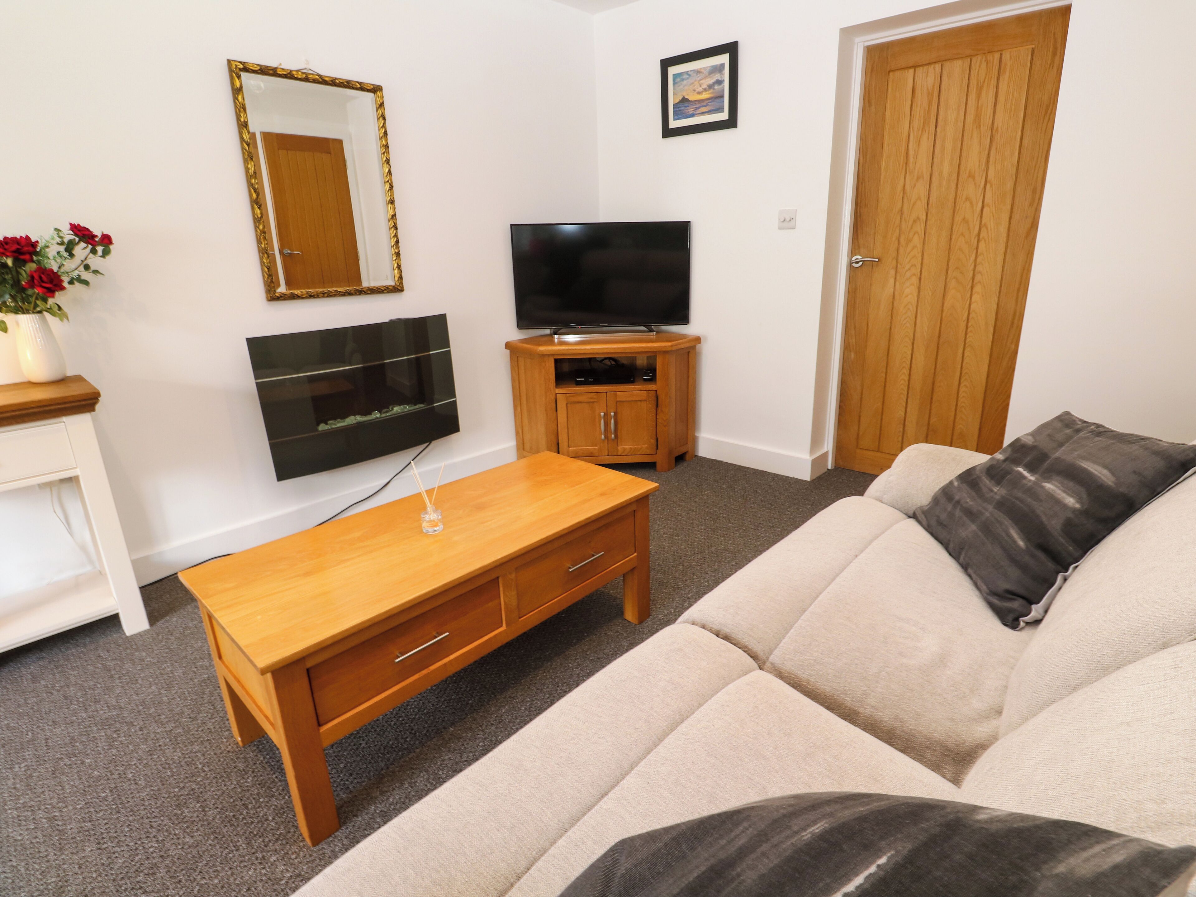 A living room with a sofa, a wooden coffee table, a TV, a cabinet, a mirror, and a door.