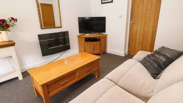 A living room with a sofa, a wooden coffee table, a TV, a cabinet, a mirror, and a door.