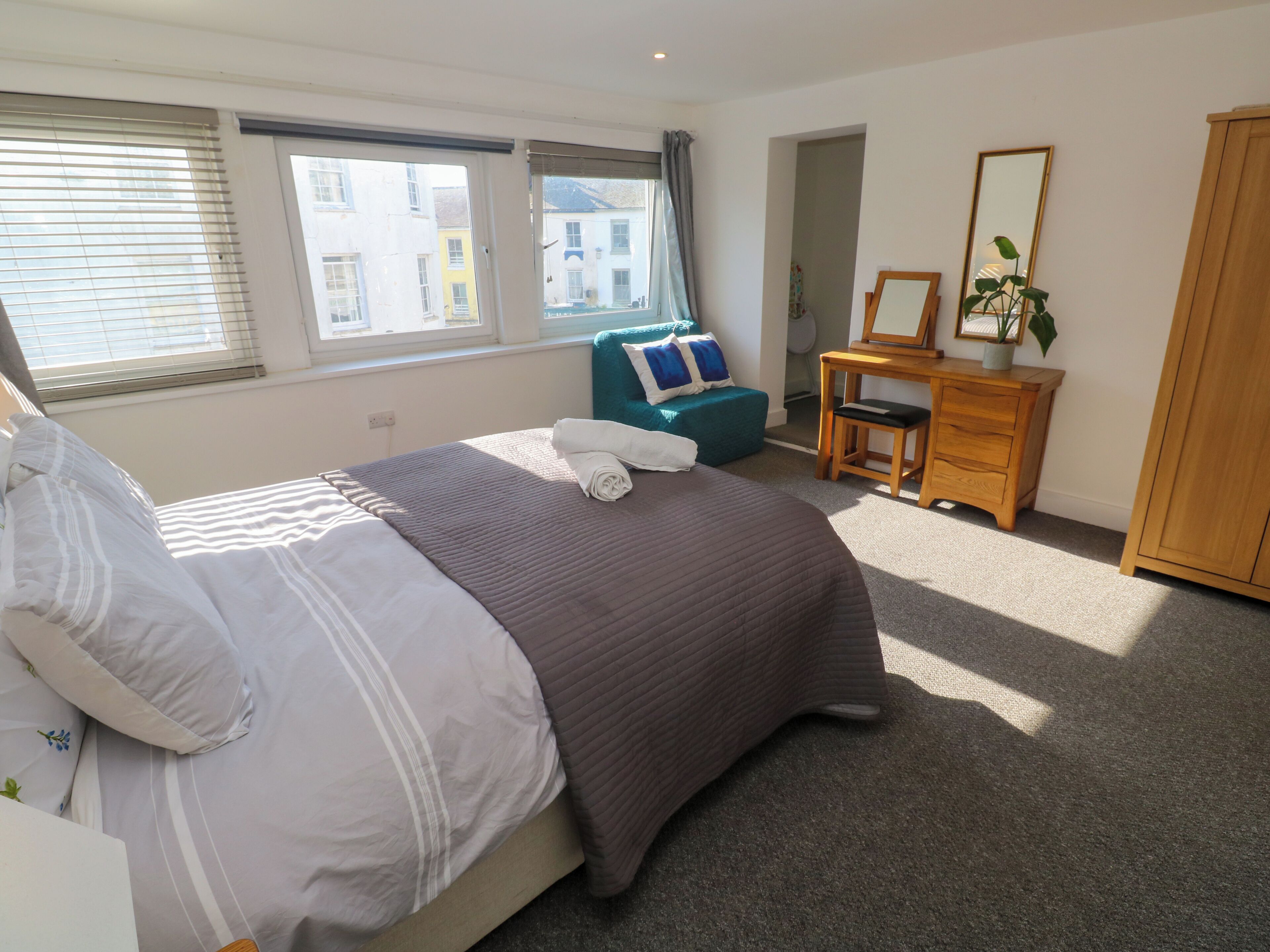 Een slaapkamer met een bed, een bureau, een stoel, een spiegel en uitzicht op gebouwen.