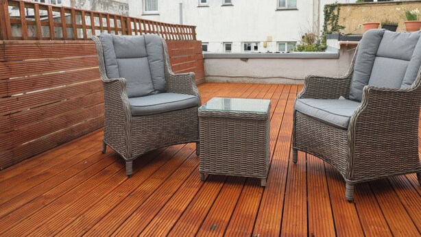 Une terrasse en bois avec des meubles en osier et une table en verre.