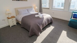 Une chambre bien rangée, avec un lit, une table de chevet et une fenêtre équipée de stores.