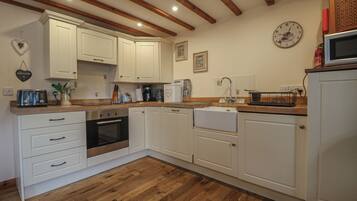 A kitchen with white cabinets, wooden flooring, a built-in oven, and a microwave.