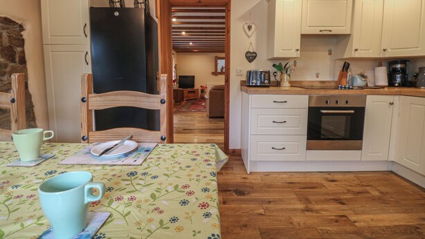 Une cuisine chaleureuse avec des meubles en bois, une table à manger recouverte d’une nappe à motifs floraux et un réfrigérateur.