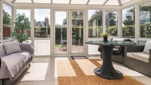 A conservatory with a glass table, sofas, and a view of the garden. - Palm Court (Carnforth)