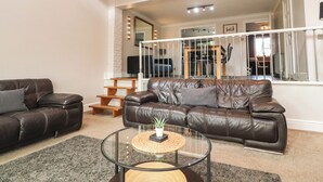 A living room with a brown leather sofa, a glass coffee table, and a wooden side table. - Palm Court (Carnforth)
