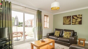 A living room with a sofa, coffee table, and a TV. There is a sliding glass door leading to an outdoor area with a patio table and umbrella.