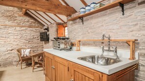 A rustic kitchen with stone walls, wooden beams, a built-in sink, and a toaster on the counter. - The Cow Cott (Hereford)