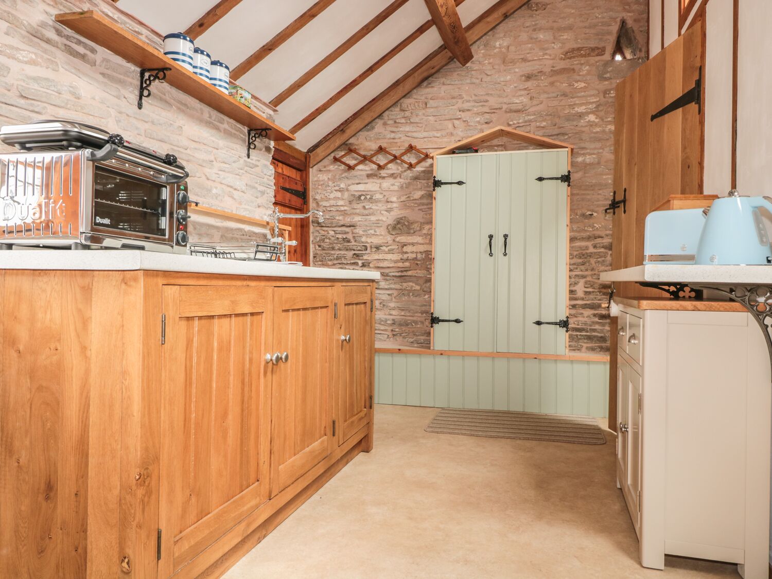 A rustic kitchen with wooden cabinets, a stone wall, and a lofted ceiling.
