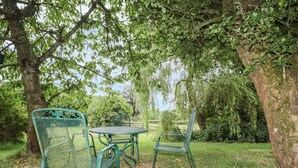 An outdoor seating area with metal chairs and a table, surrounded by trees and greenery. - The Cow Cott (Hereford)